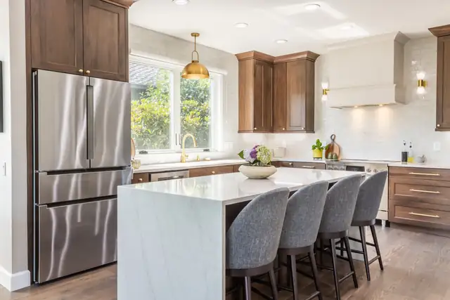 Bethany kitchen remodel in Portland with white waterfall island, gray upholstered stools and walnut upper cabinets
