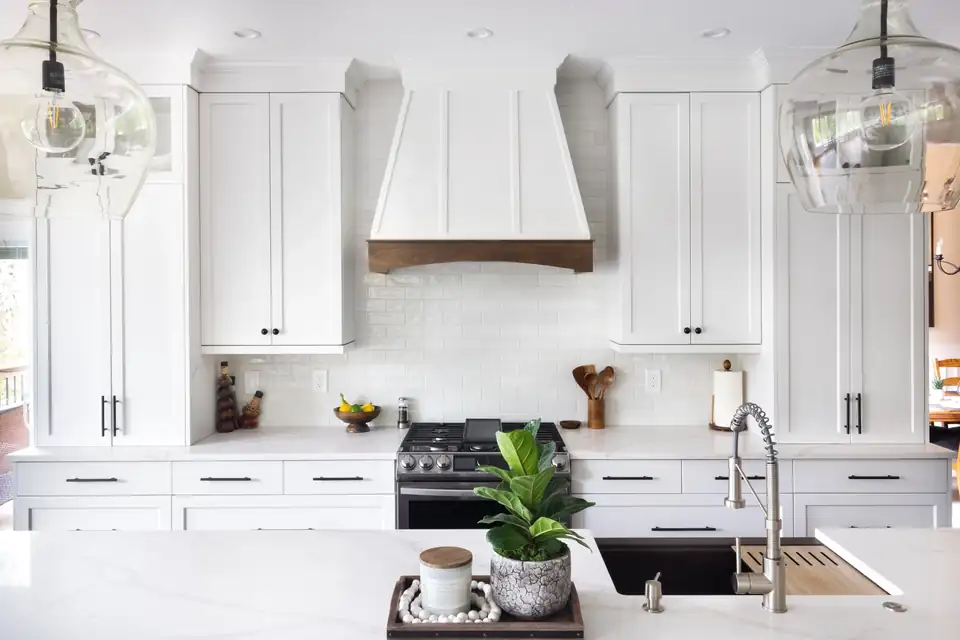 Kitchen remodeling Lake Oswego: white shaker cabinets to the ceiling, white range hood with a wood trim band, apron-front sink and glass pendant lights