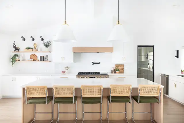 White kitchen by Straight Line with a long island, cane counter stools, white pendant lights and open shelving